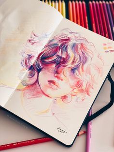 an open notebook with colored pencils and a drawing of a child's face