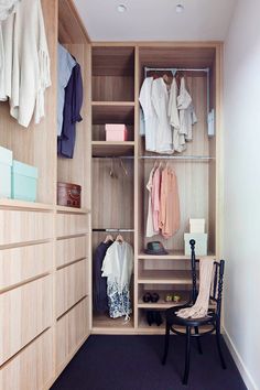 a wooden closet with clothes hanging on the shelves and a chair in front of it