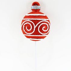 a red ornament with white swirls on a stick