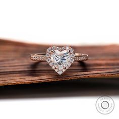 a heart shaped diamond ring on top of a wooden surface