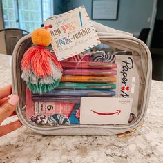 someone is holding their lunch bag full of pens and pencils, including an orange pom - pom