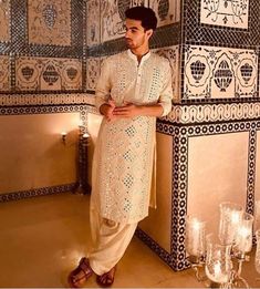 a man standing in front of a wall with decorative tiles and candles on the floor