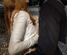 a man and woman sitting next to each other on the ground near a body of water