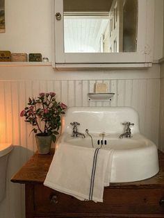 a white sink sitting under a bathroom mirror next to a wooden table with flowers on it