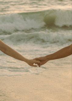 two people holding hands on the beach with waves crashing in the backgroound