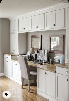 a home office with white cabinets and wood flooring is pictured in this image, there are two framed pictures on the desk