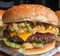 two hamburgers with cheese, lettuce and pickles on a tin foil tray