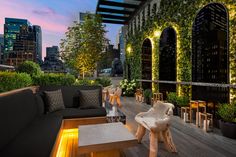 an outdoor living area with couches, tables and plants on the roof terrace at dusk