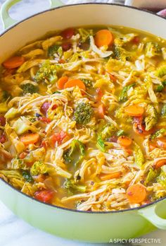 a large pot filled with pasta and vegetables on top of a white table next to a spoon