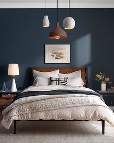 a bedroom with blue walls, white bedding and two lamps hanging from the ceiling