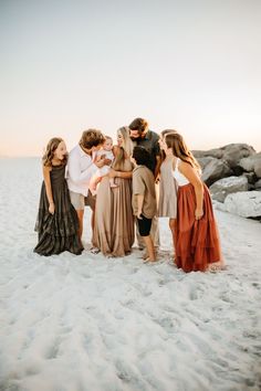 a group of people standing on top of a beach next to each other holding a baby