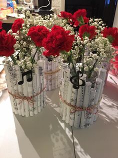 red carnations and white baby's breath are in vases made out of sheet music