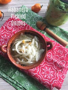 a bowl filled with onions on top of a red and green napkin next to a jar of pickled onions