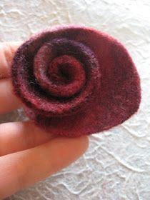 a hand holding a small red felt flower on top of a white cloth covered surface