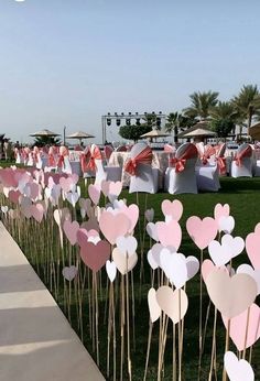 there are many hearts on sticks in the grass near some chairs and umbrellas at an outdoor event