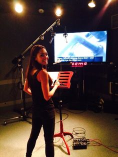 a woman standing in front of a microphone holding a piece of paper and looking at the camera