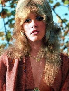 a woman with long blonde hair and blue eyes is posing for a photo in front of a tree