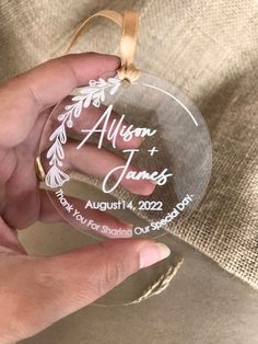 a person holding a glass ornament with the names of their wedding and date