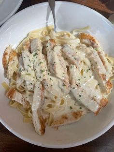 a white plate topped with pasta and chicken covered in gravy on top of a wooden table