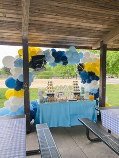 a blue and yellow birthday party under a covered area with balloons, cake and decorations