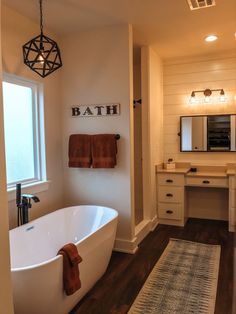 a white bath tub sitting next to a bathroom sink under a mirror and light fixture