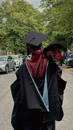 a person wearing a graduation cap and gown walks down the street in front of parked cars