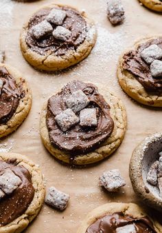 cookies with chocolate frosting and marshmallows on a baking sheet covered in powdered sugar