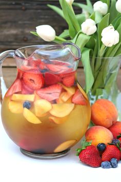 a pitcher filled with fruit sitting next to some flowers