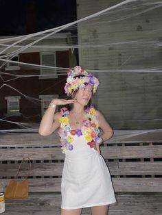 a woman in a white dress with flowers on her head standing next to a fence