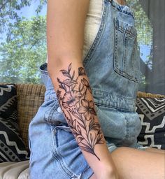 a woman with a flower tattoo on her arm sitting on a couch in front of a window