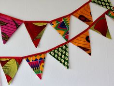 colorful flags are hanging on the wall with white walls behind them and one is red