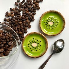 two bowls filled with green liquid next to coffee beans and spoons on a white surface