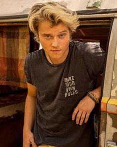 a young man leaning on the door of a van with his hand in his pocket