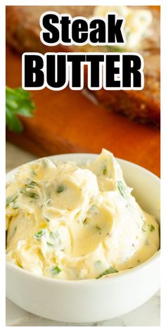 a white bowl filled with mashed potatoes on top of a wooden cutting board next to meat