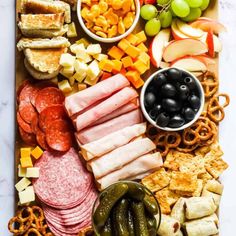 an assortment of meats, cheeses, crackers and fruit on a cutting board