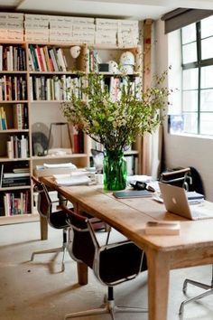 a wooden table topped with a laptop computer next to a book shelf filled with books