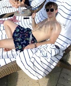 a man laying on top of a beach chair next to another person wearing sunglasses and holding a drink