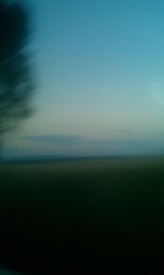 a blurry photo of the sky and trees from a train window at dusk or dawn