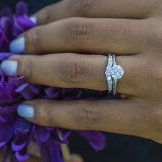 a close up of a person's hand with a ring on it and purple flowers in the background