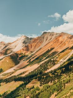 the mountains are covered in snow and green trees, with clouds above them on a sunny day