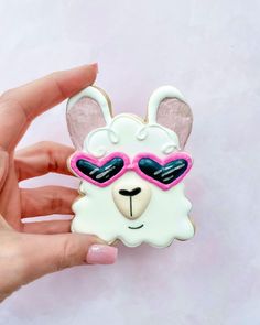 a hand holding a white and pink llama with sunglasses on it's face