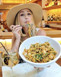 a woman in a hat is eating pasta with chopsticks and a glass of wine