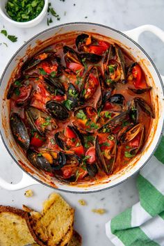 a pot filled with mussels and tomatoes on top of a table next to bread