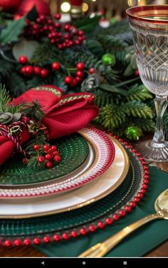 a table set for christmas with red and green plates, silverware and greenery