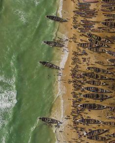 several boats are lined up on the shore by the water's edge as people walk along the beach