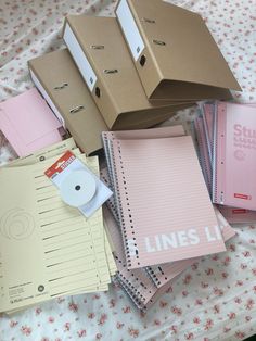 several binders and boxes on a bed with pink flowers in the background, including lined notebooks