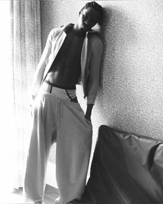 a black and white photo of a man leaning against a wall with his shirt open