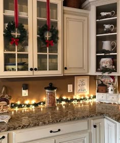 a kitchen decorated for christmas with lights and wreaths on the cabinet doors, along with other holiday decorations