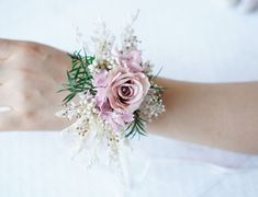 a person's hand holding a pink and white flower bouquet with greenery on it