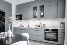 a kitchen with grey cabinets and white chairs is shown in this image, there are vases on the table next to the stove